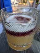 A yellow cocktail in a rocks glass deep red layer of wine floating on top.